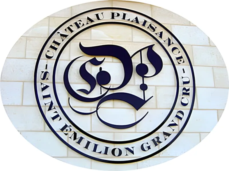 A circular metal logo mounted on a white stone wall featuring ornate \