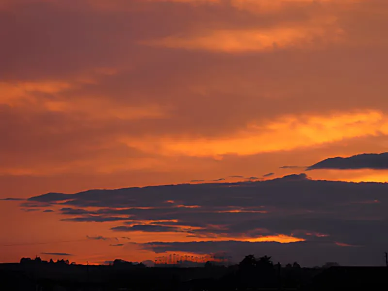 A dramatic sunset with vibrant orange and red clouds stretching across the sky over a silhouetted landscape.