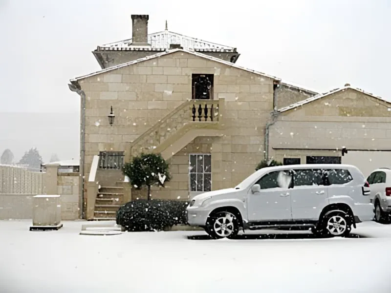 Ein Steinhaus mit einem silbernen SUV davor geparkt, mit leichtem Schneefall rundherum.