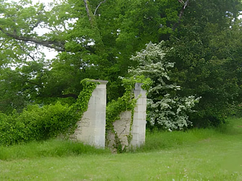 Two weathered stone pillars standing in a green field surrounded by trees, marking the entrance to an underground cave system.