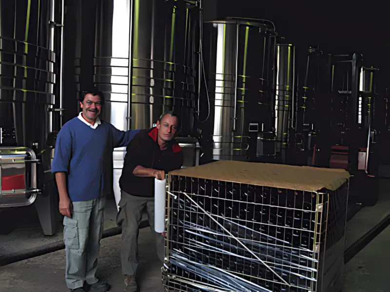 一位笑容满面的葡萄园工人在普莱桑城堡将空酒瓶装入传送带上的金属笼中。